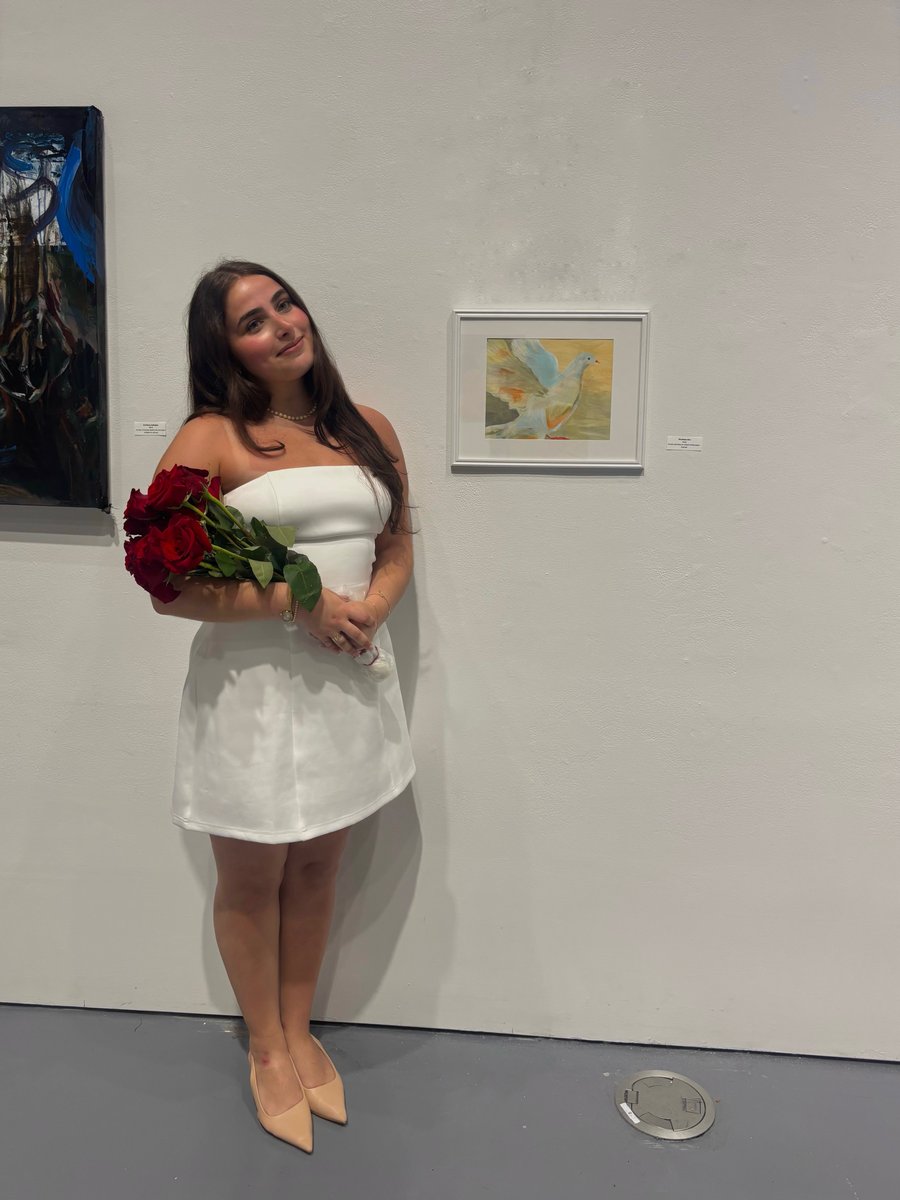 Shoshi Birn at a gallery exhibition, holding roses beside her dove painting